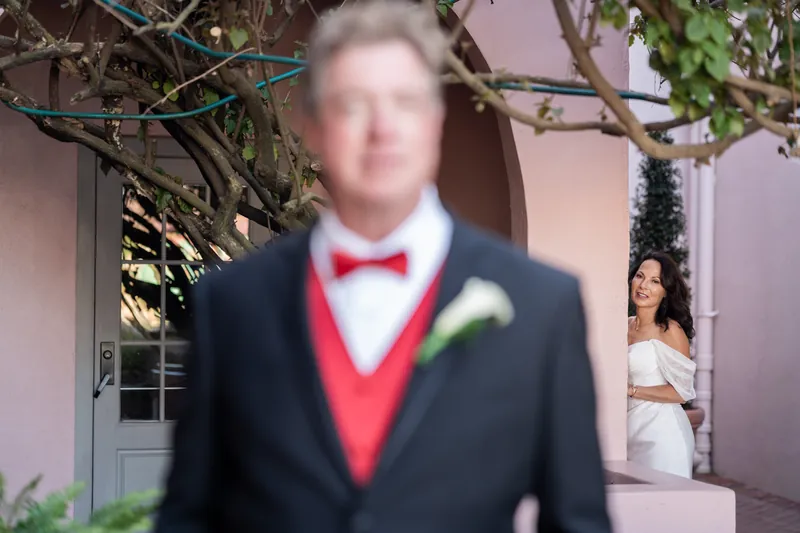 Bill stands in a black suit with red vest and bow tie outside The White Room's arched entrance.