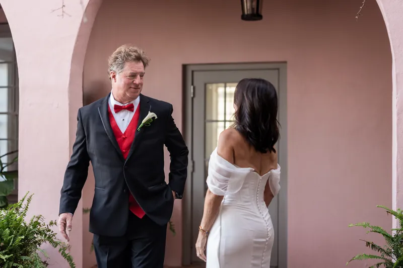 Bill and Rose Ann walk side-by-side past The White Room's pink stucco wall and arched doorway.