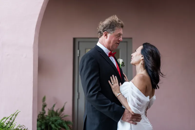 Rose Ann and Bill face each other and smile under The White Room's pink arched entrance.