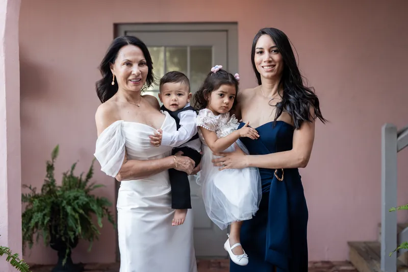 Four women in black and white dresses holding two small children at The White Room's pink courtyard.