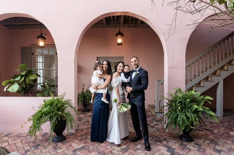 Rose Ann and Bill stand with two children under arched breezeway at The White Room's pink facade.