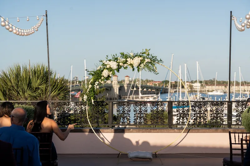 Curved floral arch with white and cream roses and greenery frames a marina view at The White Room wedding ceremony.