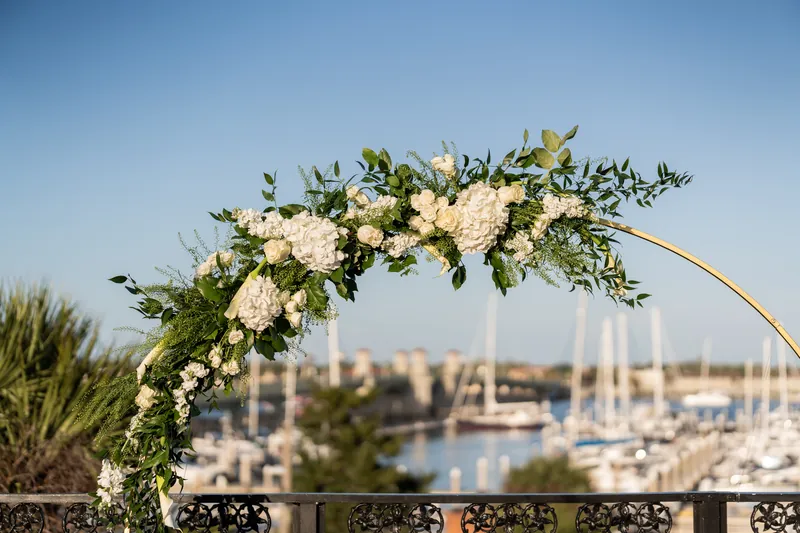 Cream-colored rose and eucalyptus floral swag draped over railing overlooks sailboats in the harbor.