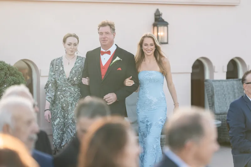Bill walks down the aisle with two family members while guests watch during the ceremony at The White Room.