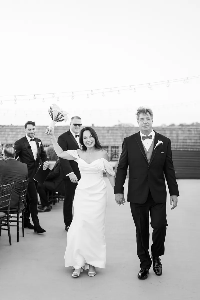 Rose Ann and Bill walk together on rooftop at The White Room, guests applauding with confetti falling.