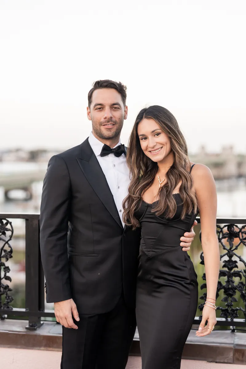 Bill in a black tuxedo with bow tie and Rose Ann in a black sleeveless dress stand together on a rooftop at The White Room.