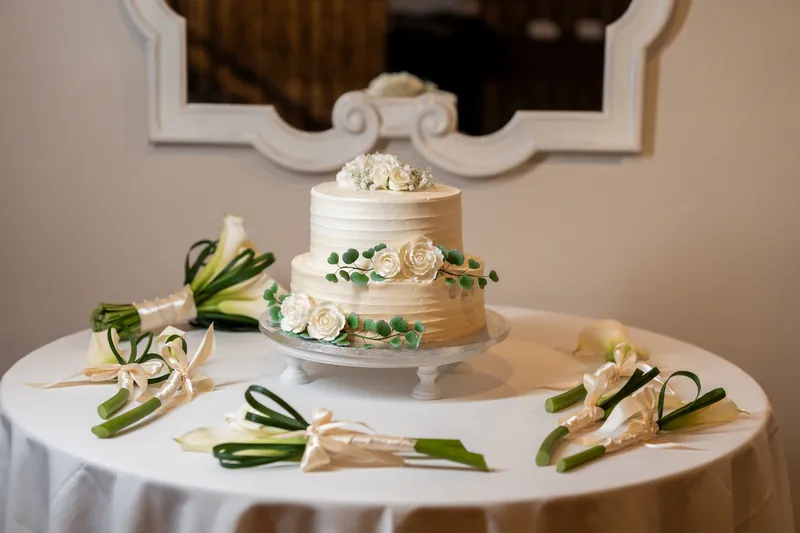 Three-tier wedding cake with white frosting, green garland, and white sugar flowers surrounded by appetizers on display table.
