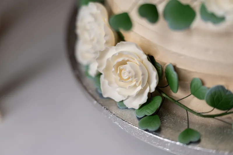 Close-up of white sugar rose and eucalyptus leaves decorating the side of the wedding cake.