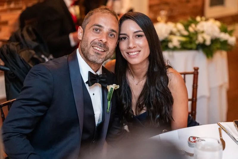 Bill wears a navy tuxedo with boutonniere while Rose Ann smiles in a white dress at The White Room reception.
