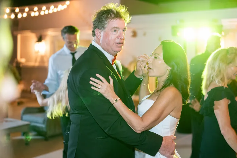 Bill hugs a female guest while dancing, with string lights and greenery visible in The White Room's event space.