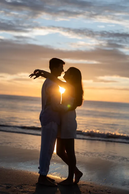 Pasha lifts Sally during a kiss on the beach with golden sunset light glowing between them.