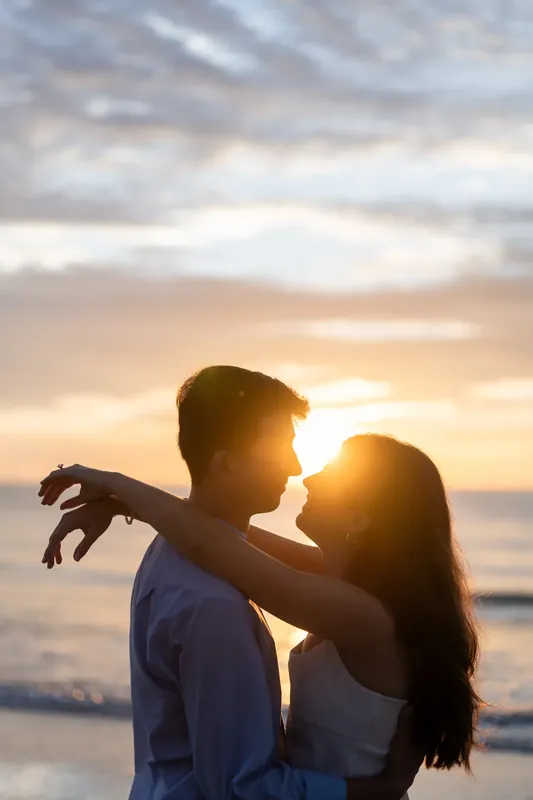 At sunset on St. Augustine Beach, Pasha holds Sally as she wraps her arm around his neck, backlit by golden sky and ocean.