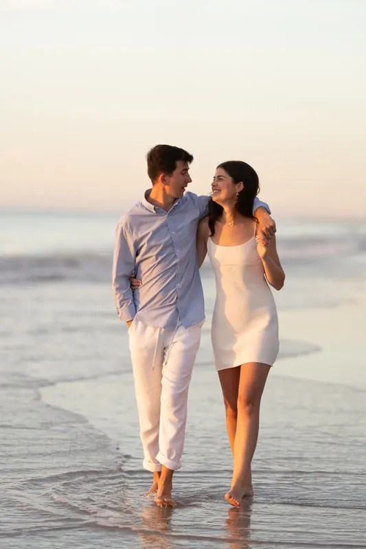 Pasha and Sally stroll along the wet sand at St. Augustine Beach, smiling at each other as golden hour light bathes them.