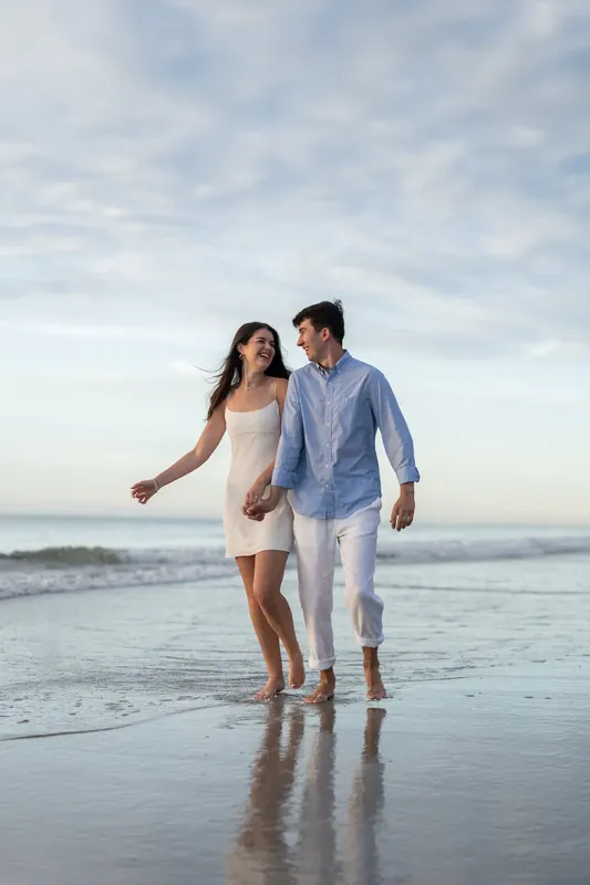 Sally extends her arm toward the ocean while walking beside Pasha through the surf at St. Augustine Beach at dusk.
