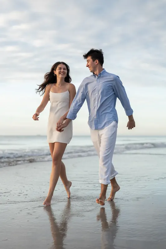 Pasha and Sally jog barefoot through shallow water on St. Augustine Beach, holding hands as the sun sets behind them.