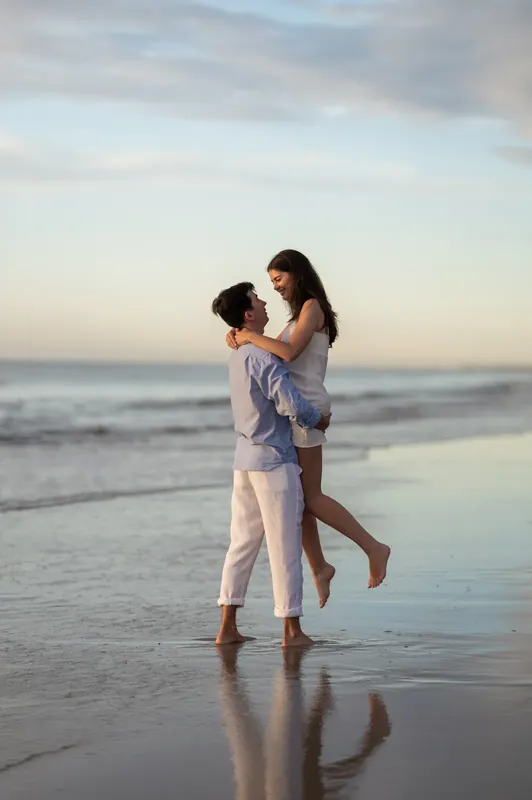 Pasha lifts Sally into his arms as they stand in shallow water at St. Augustine Beach at sunset.
