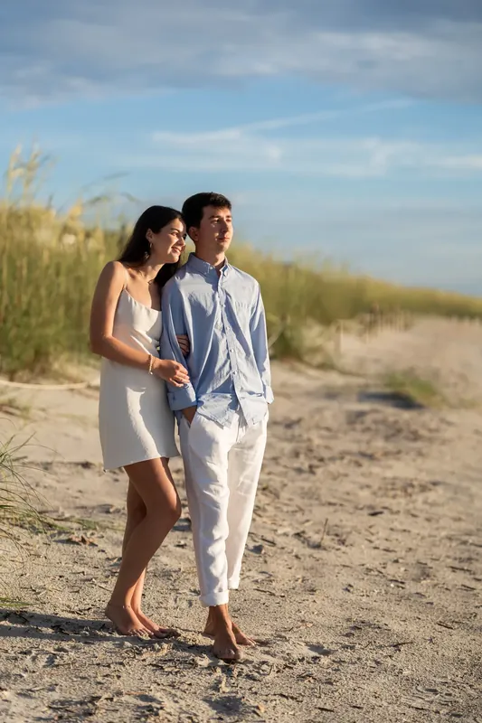 Sally and Pasha walk together along the sandy beach with dune grasses framing the scene.