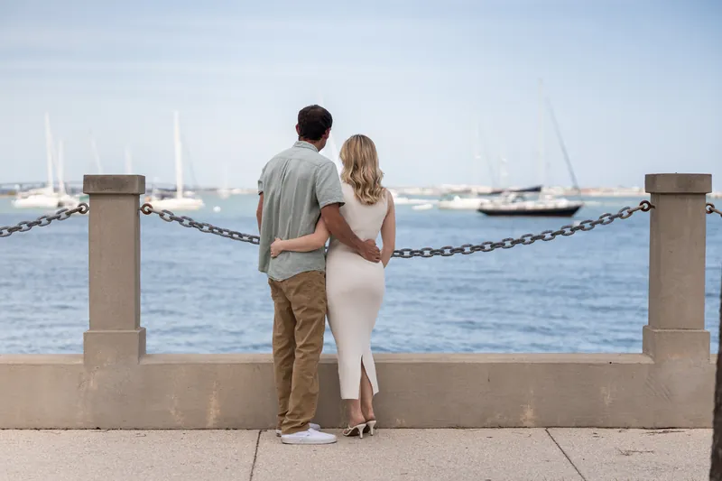 Dillon and Samantha stand at a waterfront railing overlooking sailboats in the harbor.