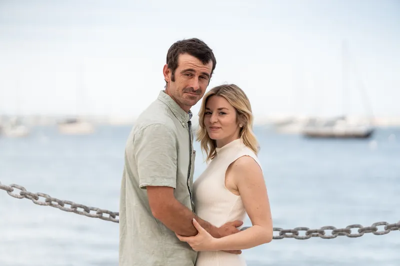 Dillon and Samantha pose together by the water with sailboats visible in the distance.