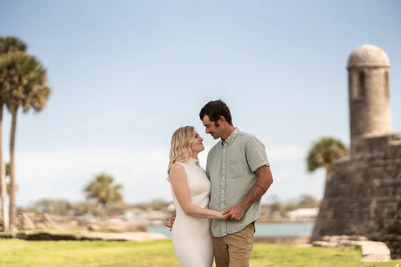 Samantha and Dillon stand facing each other on a grassy area near historic stone ruins and palm trees in downtown St. Augustine.