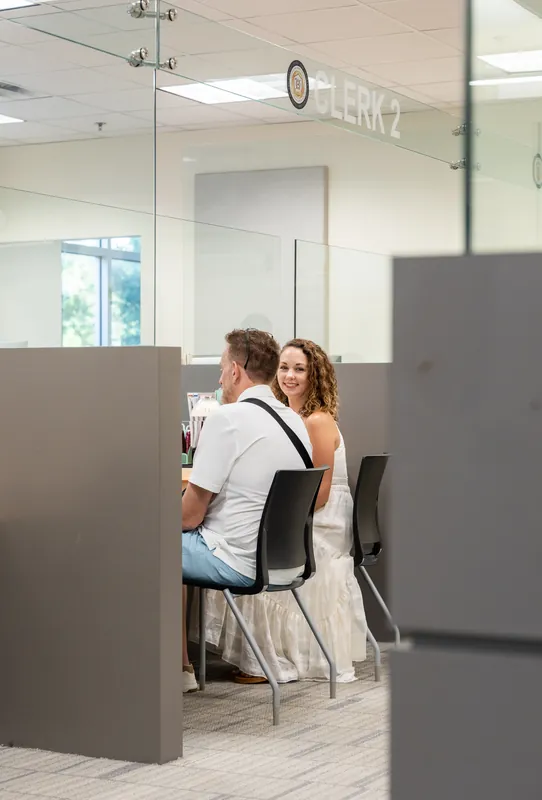 Samantha and Daniel stand at courthouse windows separated by gray partitions.