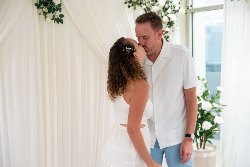 Daniel leans in to kiss Samantha after their ceremony, surrounded by flowing white fabric and hanging green garland.