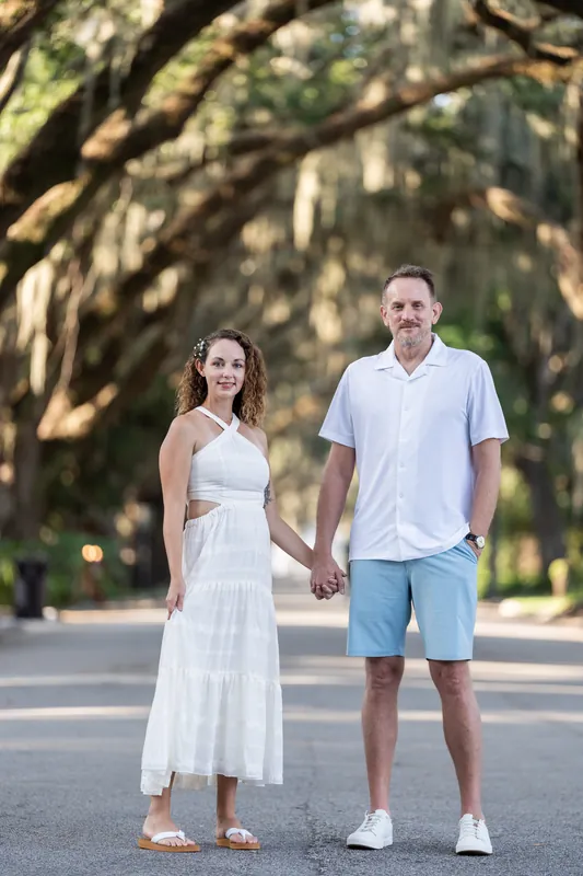 Samantha and Daniel hold hands walking under massive oak trees draped with Spanish moss.