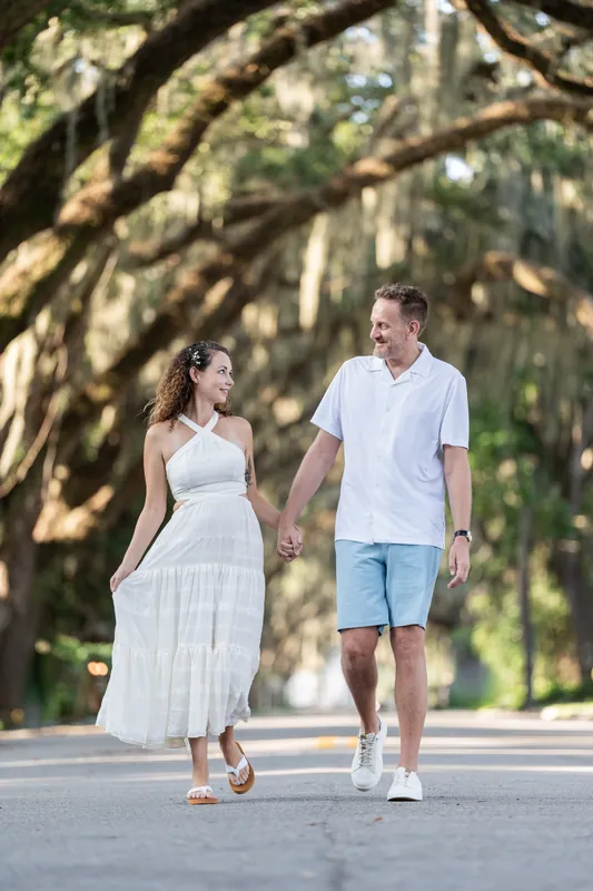 Samantha and Daniel walk hand-in-hand beneath a canopy of live oak trees draped with Spanish moss on Magnolia Avenue.