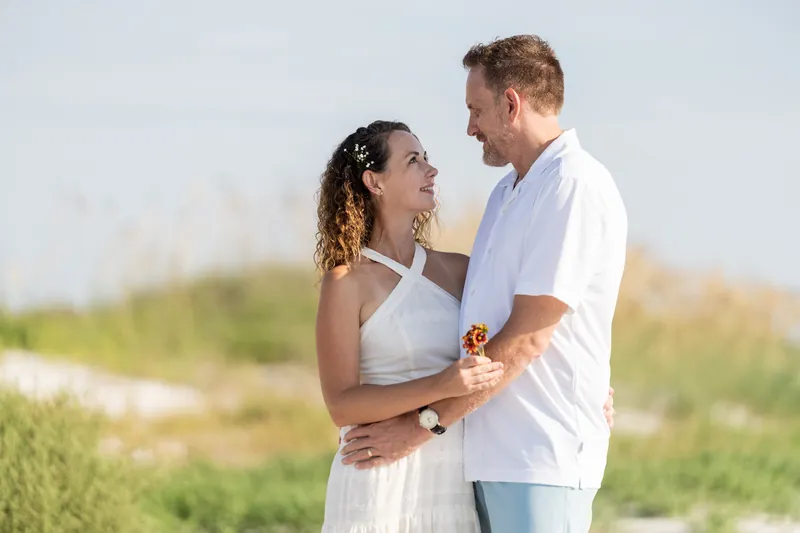Daniel and Samantha embrace face-to-face at Vilano Beach, dune grasses and sandy landscape behind them.