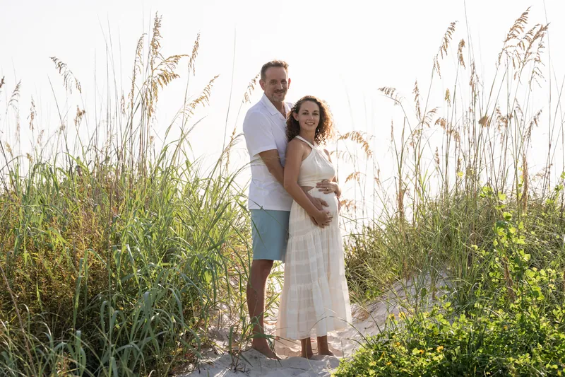 Daniel embraces Samantha among tall sea oats on the beach, both in light casual clothing.