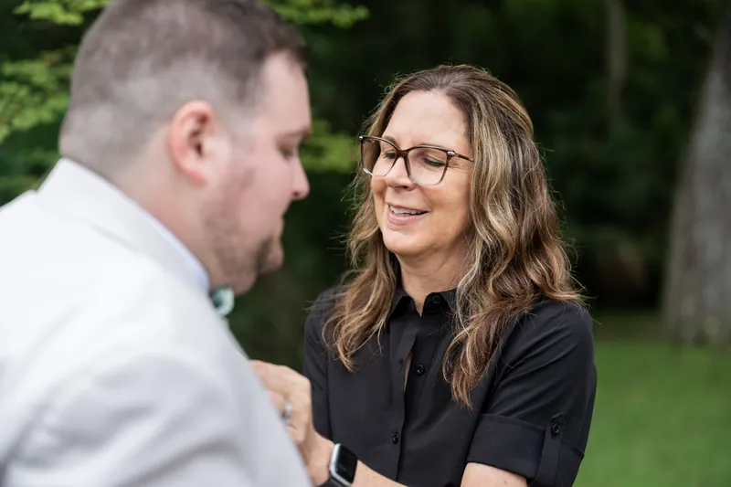 Matthew and Samantha face each other and smile during their outdoor elopement celebration surrounded by green grounds.