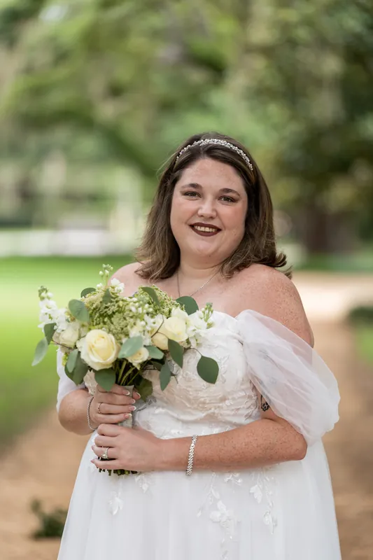 Samantha holds her white and greenery bouquet while wearing an off-shoulder white gown at the garden park.