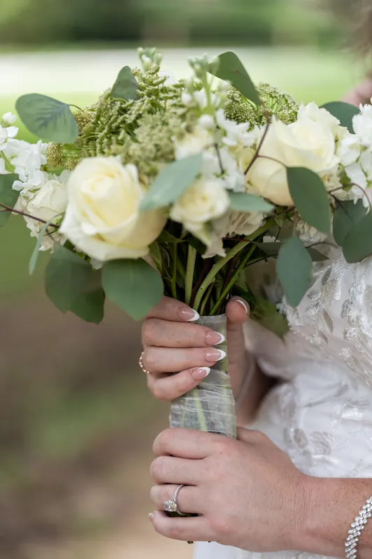 Samantha's hands display delicate rings as she holds a white rose and greenery bouquet at Washington Oaks Gardens State Park.