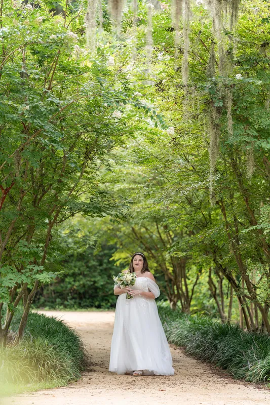 Samantha in a white dress stands alone on a sandy path beneath a canopy of moss-draped oak trees.