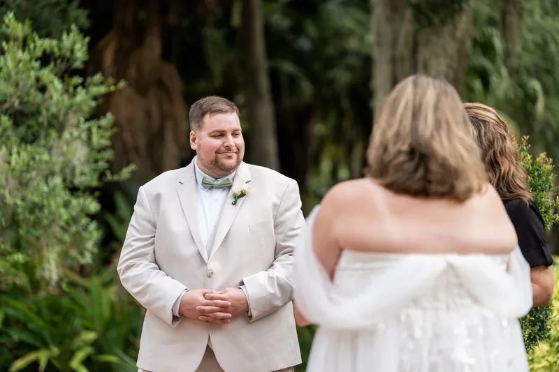 Matthew in a beige suit watches Samantha approach through Spanish moss-draped oaks at Washington Oaks Gardens State Park.
