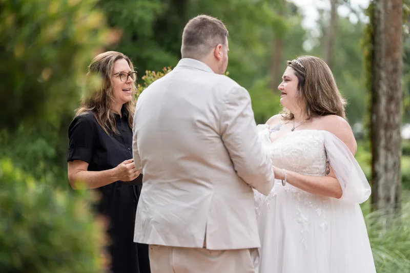 An officiant speaks with Matthew and Samantha as they stand together beneath towering oaks and Spanish moss.