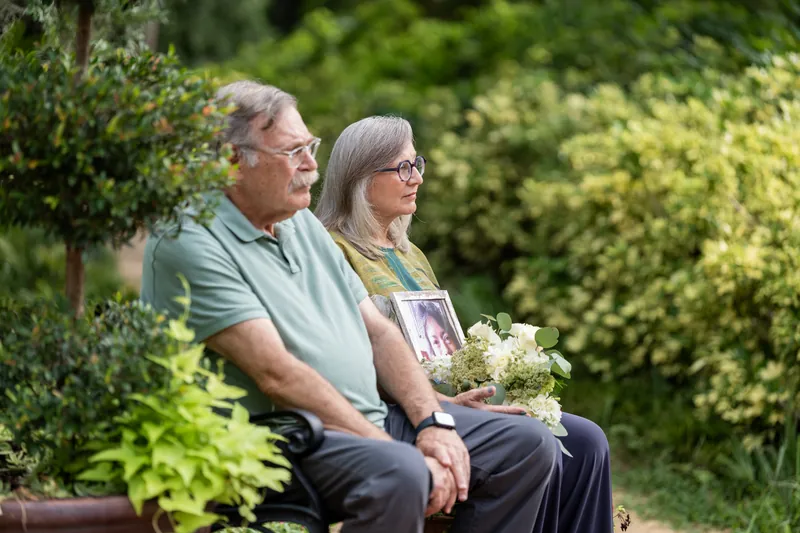 Two guests sit on a bench with a bouquet, watching the ceremony unfold amid the verdant garden setting.