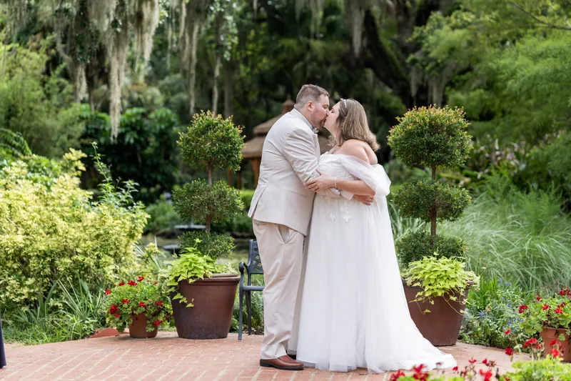 Samantha and Matthew kiss among lush greenery and potted flowers at the garden venue.