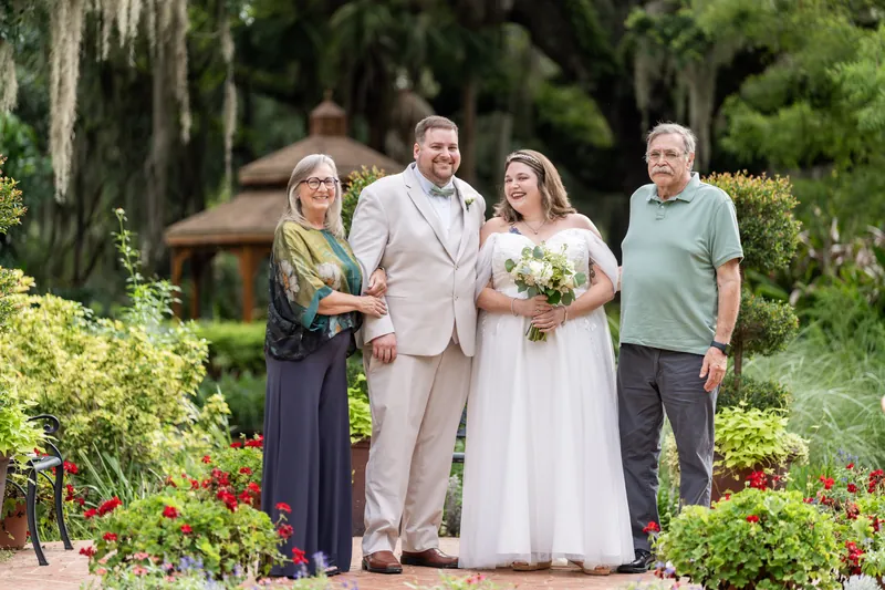 Samantha and Matthew pose with two family members in the garden, both holding the white bridal bouquet.