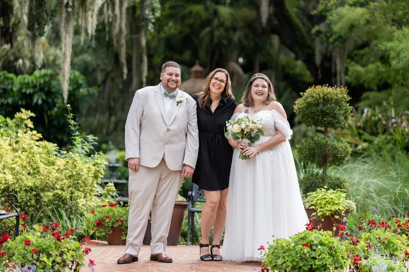 Matthew and Samantha stand with their officiant among flowering beds and moss-draped oaks at Washington Oaks Gardens.