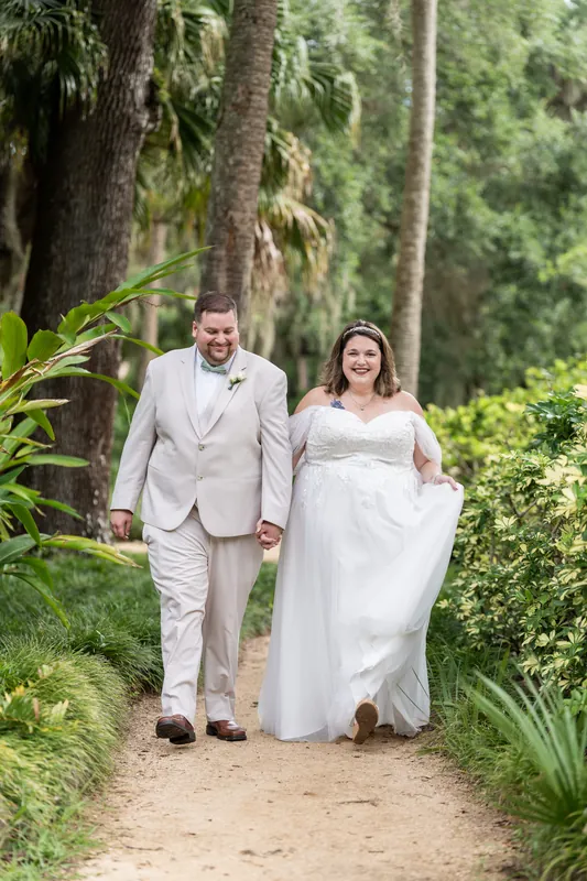 Samantha and Matthew walk a dirt path through palmettos, her white dress flowing behind them.