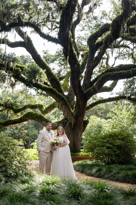 Standing beneath a massive, sprawling oak tree, Samantha holds her bouquet while Matthew wraps an arm around her.