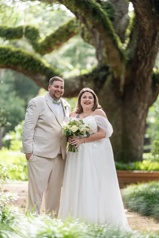 Matthew places his hand on Samantha's shoulder as they stand together under moss-draped branches, both smiling warmly.