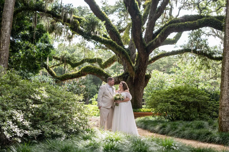 The couple poses beneath an ancient oak, its massive limbs creating a natural canopy above them in the garden.