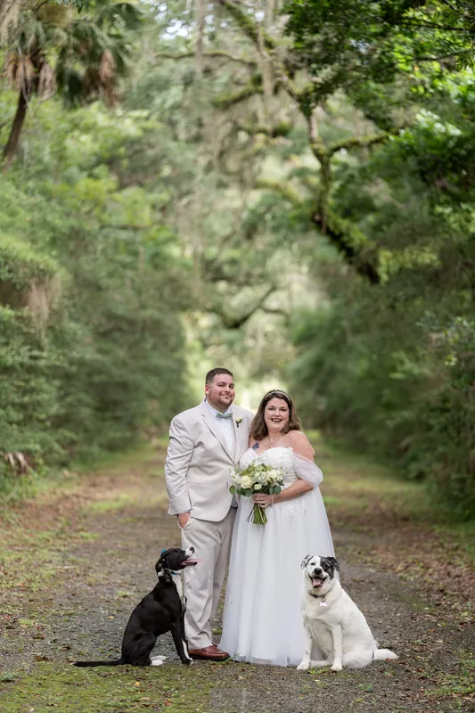 Matthew and Samantha pose together with two dogs at their feet beneath a canopy of oak trees.