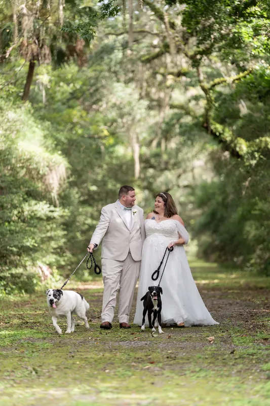 Matthew, Samantha, and two dogs stand together on a grassy path lined with dense green foliage overhead.