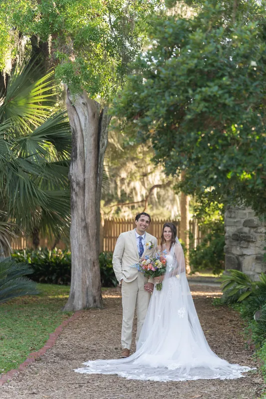 Phil and Sammy kiss beneath her billowing veil, dappled sunlight dancing across their faces as they embrace in the park's