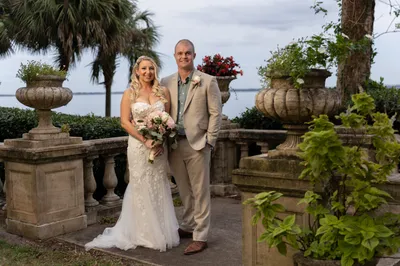 Bride and groom posing together in elegant garden with water view and classical urns