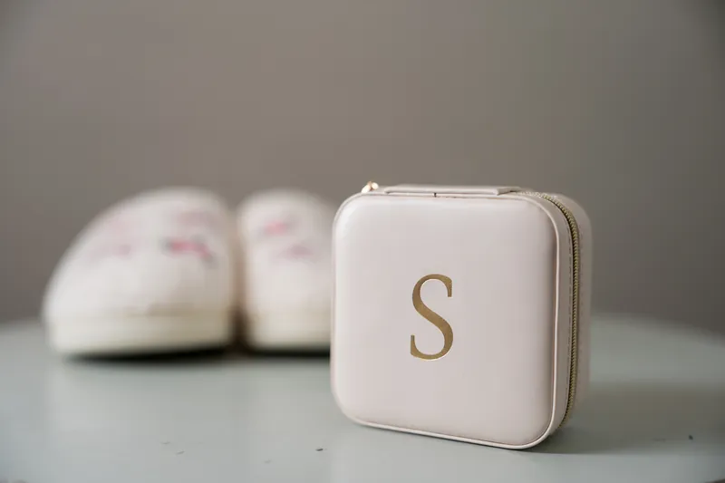 Monogrammed jewelry box with the letter "S" in gold sits on a gray surface beside blurred white shoes.