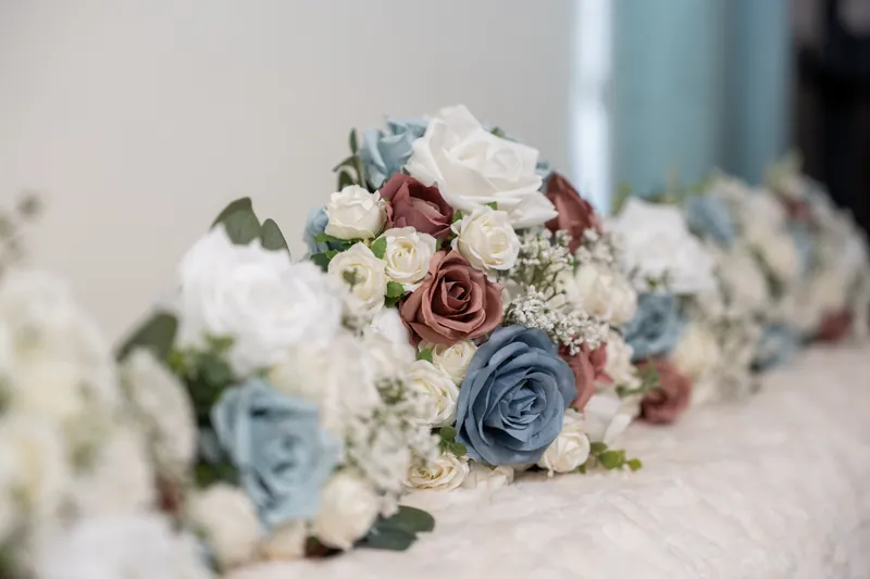 Four bridal bouquets with dusty blue, mauve, and cream roses and white filler flowers arranged in a row.